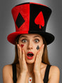 Eine Frau trägt den „Casino Stoff Zylinder schwarz-rot“, einen auffälligen schwarz-roten Zylinder, der mit Kartensymbolen verziert ist, dazu passend ist ihr Gesicht mit den entsprechenden Kartensymbolen bemalt. Mit den Händen an den Wangen sieht sie überrascht aus – das perfekte Outfit für eine Las-Vegas-Party.