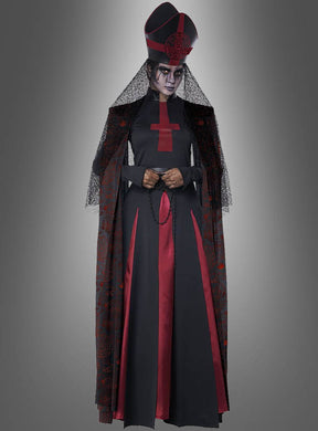 Eine Person in einem schwarz-roten, von einer Bischöfin inspirierten Kostüm mit Schleier, großem Kopfschmuck und einem roten Kreuz auf dem Kleid, die einen Rosenkranz in der Hand hält – dieses auffällige „Dunkle Priesterin“-Halloween-Kostüm hebt sich deutlich von einem grauen Hintergrund ab.