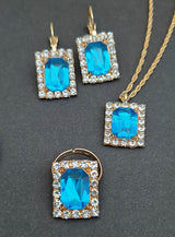 Klar! Hier ist eine überarbeitete Version mit Ihren Produktdaten: Das „Edles Schmuckset mit Edelsteinen und Strass“ besteht aus Goldschmuck, der mit rechteckigen blauen Edelsteinen verziert ist, die jeweils von funkelnden klaren Steinen umrahmt werden. Dieses elegante Set umfasst eine Halskette, passende Ohrringe und einen Ring – alles wunderschön vor einem dunklen Hintergrund präsentiert. Ideal als Kostümschmuck, um jedem Outfit einen Hauch von raffinierter Eleganz zu verleihen.