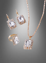 Edles Schmuckset mit Edelsteinen und Strass: Dieses elegante Set besteht aus einer Halskette mit rechteckigem Anhänger, passenden Ohrringen und einem Ring, jeweils mit einem großen, klaren Edelstein, umgeben von funkelnden Strasssteinen auf grauem Hintergrund – perfekt für jeden Anlass.