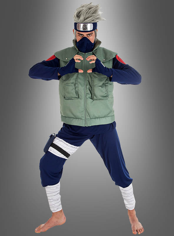 Eine Person, die das Kakashi-Kostüm aus „Naruto“ trägt – bestehend aus einer grünen Weste, einem blauen Outfit, einem Stirnschutz und einer Maske –, posiert barfuß in einer Kampfkunsthaltung, die von „Naruto Shippuden“ inspiriert ist.