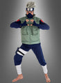 Eine Person, die das Kakashi-Kostüm aus „Naruto“ trägt – bestehend aus einer grünen Weste, einem blauen Outfit, einem Stirnschutz und einer Maske –, posiert barfuß in einer Kampfkunsthaltung, die von „Naruto Shippuden“ inspiriert ist.