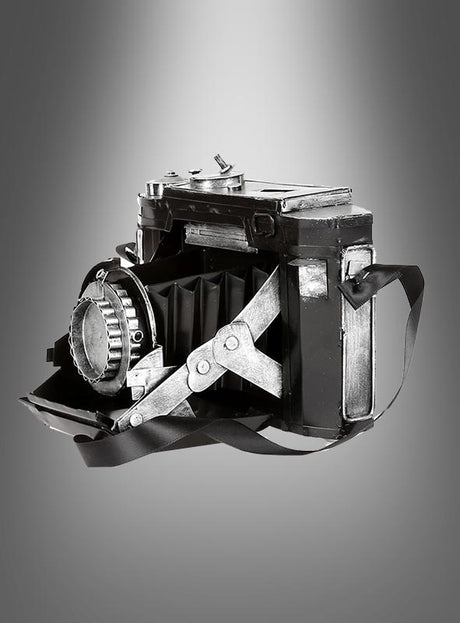 Eine Vintage-Fotokamera-Dekoration aus Blech mit Trageriemen, präsentiert vor einem grau abgestuften Hintergrund, eignet sich ideal als Vintage-Dekorationsstück oder als authentische Vintage-Fotokamera für jedes Kostüm-Ensemble im Stil der 20er Jahre.