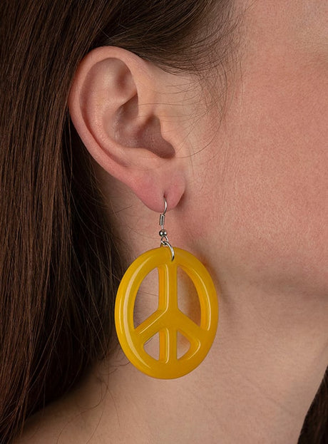 Nahaufnahme des Ohrs einer Person, die einen großen gelben Hippie-Ohrring „Peace“ trägt, der wie ein Friedenssymbol geformt ist – perfekt, um jedes Hippie-Kostüm abzurunden.