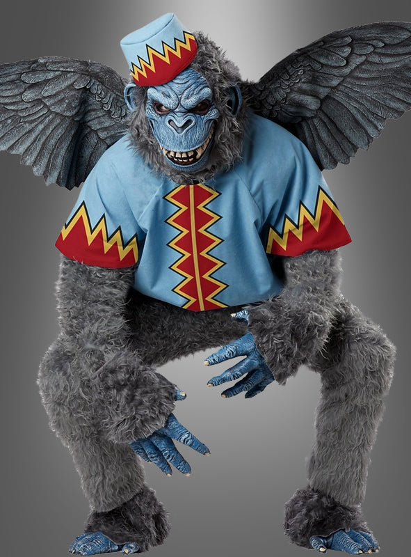 Die Person, die das „Fliegender Affe“-Märchenkostüm Deluxe trägt, ist in ein blau-rotes Outfit mit Zickzack-Borte gekleidet, hat eine Affenmaske und einen passenden Hut auf und ist mit blauer Gesichtsbemalung vor einem grauen Hintergrund in die Hocke gegangen.