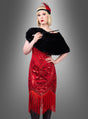 Eine Person, die das „Luxuriöse Kleid mit Pailletten Cleo“ trägt – ein rotes Flapper-Kleid mit Fransen, das an ein glamouröses Cocktailkleid erinnert –, kombiniert mit einer schwarzen Pelzstola und einem schwarzen Stirnband, das mit einer roten Feder verziert ist, hält eine Zigarettenspitze vor einem grauen Hintergrund mit Farbverlauf.