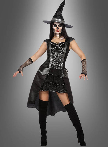 Eine Person trägt das „Rockiges Hexenkostüm“ – bestehend aus einem schwarzen Spitzhut, einem korsettartigen Vokuhila-Kleid, Handschuhen und Stiefeln – sowie eine von Skeletten inspirierte Gesichtsbemalung und posiert vor einem grauen Hintergrund mit Farbverlauf.