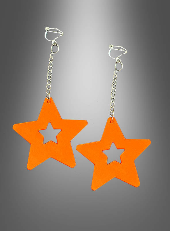 Ein Paar Ohrhänger aus der Kollektion „80er Clip-Ohrringe Neon Blitz oder Sterne“ mit auffälligen orangefarbenen, sternförmigen Anhängern mit Aussparung in der Mitte, die an silbernen Ketten vor einem grauen Hintergrund hängen. Dieses auffällige Design fängt den pulsierenden Geist des legendären 80er-Jahre-Schmucks ein und verleiht ihm einen Neon-Touch, der von klassischem 80er-Jahre-Schmuck inspiriert ist.