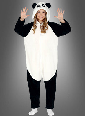 Ein Kind steht mit dem Gesicht nach vorne und trägt einen „Panda-Overall für Kinder“ – einen kuscheligen schwarz-weißen Strampler mit Kapuze, die Pandaohren und -augen hat. Es hat die Arme erhoben und lächelt.