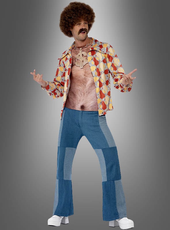 Ein Mann in einem Retro-Outfit aus den 1970er Jahren trägt das T-Shirt „Lustiges 70er Brusthaare“ und präsentiert komische Brusthaare, als wären sie echt. Dazu trägt er Patchwork-Jeans, weiße Plateauschuhe und eine Afro-Perücke – er posiert vor einem grauen Hintergrund mit Farbverlauf – perfekt für jede 80er-Jahre-Party.