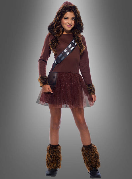 Ein Kind im Chewbacca-Kostüm für Mädchen – Star Wars, mit braunen, pelzigen Details, einem verspielten Tutu-Rock und einem bedruckten Schulterriemen, steht vor einem grauen Hintergrund. Dieses einzigartige Wookiee-Kostüm eignet sich perfekt als Star-Wars-Kinderkostüm für junge Fans.