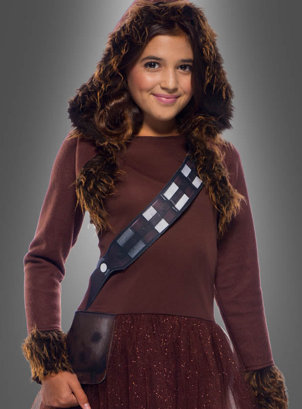 Ein Mädchen, das das „Chewbacca-Kostüm für Mädchen – Star Wars“ trägt – aus braunem Stoff mit Pelzbesatz, einer Kapuze und einem Riemen im Bandolier-Stil über der Brust –, steht vor einem grauen Hintergrund.