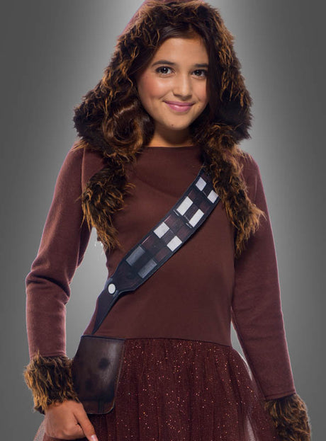 Ein Mädchen, das das „Chewbacca-Kostüm für Mädchen – Star Wars“ trägt – aus braunem Stoff mit Pelzbesatz, einer Kapuze und einem Riemen im Bandolier-Stil über der Brust –, steht vor einem grauen Hintergrund.