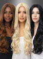 Drei Frauen mit langen, welligen Haaren – eine mit braunen Haaren, eine mit platinblonden Haaren und eine mit schwarzen Haaren – stehen nebeneinander vor einem grauen Hintergrund mit Farbverlauf und tragen jeweils die Langhaar-Perücke „Wellig Chrissy“, die sich ideal für jedes Hippie-Kostüm oder jeden festlichen Anlass eignet.