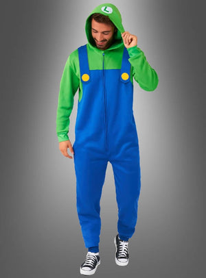 Eine Person, die einen grünen Kapuzenpulli und den „Luigi-Overall für Erwachsene“ trägt – ein blaues Kostüm mit gelben Knöpfen, inspiriert von der legendären Super-Mario-Spielfigur –, steht vor einem grauen Hintergrund mit Farbverlauf, wodurch es sich perfekt für Fasching-Feiern eignet.