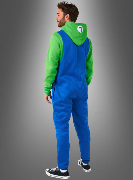 Ein Mann steht vor einem Hintergrund mit Farbverlauf und trägt den „Luigi-Overall für Erwachsene“, kombiniert mit einem grünen Hoodie, auf dessen Kapuze ein weißer Kreis und die Zahl 1 zu sehen sind – eine ideale Wahl für den Fasching oder als Teil eines Super-Mario-Kostüms –, dazu schwarze Sneaker; er steht mit dem Rücken zur Kamera.