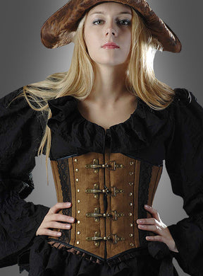 Eine Frau mit einem braunen Piratenhut, einer schwarzen Rüschenbluse und dem „Antiklook Korsage braun Steampunk“-BH mit Metallschnallen und Wildlederoptik, die mit den Händen in den Hüften vor einem grauen Hintergrund posiert.