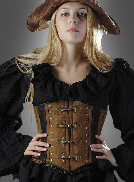 Eine Frau mit einem braunen Piratenhut, einer schwarzen Rüschenbluse und dem „Antiklook Korsage braun Steampunk“-BH mit Metallschnallen und Wildlederoptik, die mit den Händen in den Hüften vor einem grauen Hintergrund posiert.