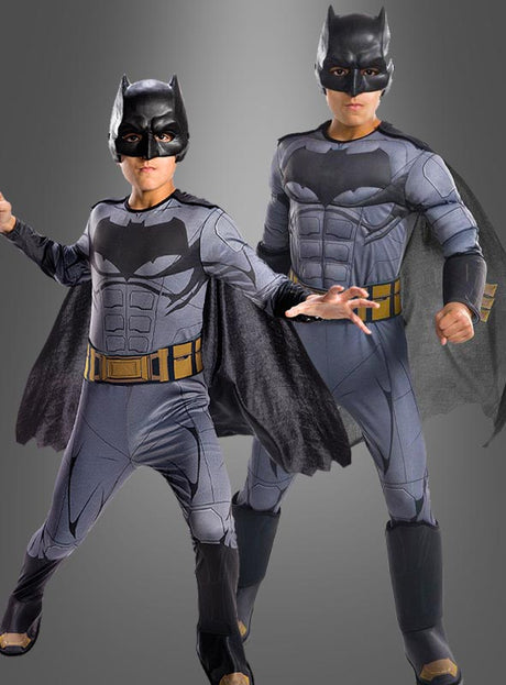 Zwei Kinder, die das Batman-Filmkostüm aus „Justice League“ tragen – komplett mit Masken, Umhängen und Ausrüstungsgürteln –, stehen selbstbewusst vor einem grauen Hintergrund mit Farbverlauf. Dieses offizielle DC-Comics-Lizenzprodukt ist ideal für junge Superhelden, die der Justice League beitreten möchten.