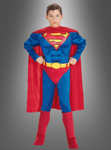 Ein Kind, das das Original-Superman-Kinderkostüm trägt – bestehend aus einem roten Umhang, einem blauen Anzug, roten Stiefeln und einem gelben Gürtel –, steht mit den Händen in den Hüften da.