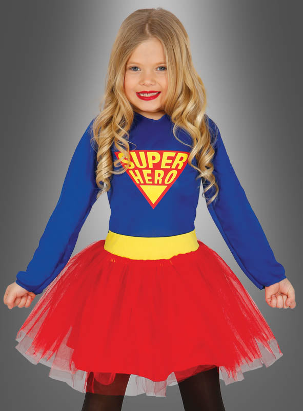 Ein junges Mädchen mit langen blonden Haaren trägt das „Superheldin“-Kinderkostüm – ein blaues Oberteil mit der Aufschrift „SUPER HERO“ und einen roten Tutu-Rock – und steht vor einem grauen Hintergrund mit Farbverlauf, was es zum perfekten „Superheldin“-Kostüm für Mädchen macht.
