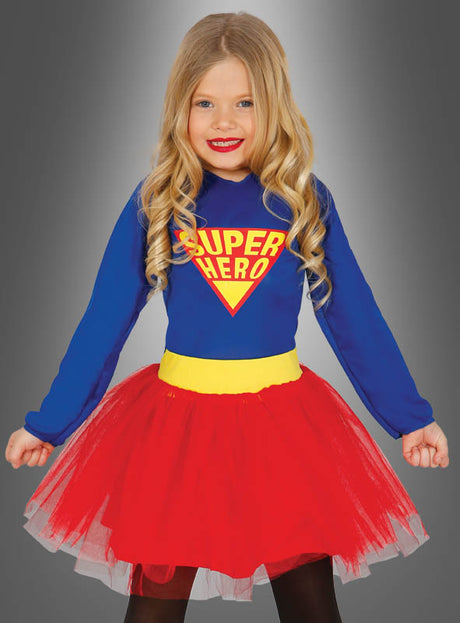 Ein junges Mädchen mit langen blonden Haaren trägt das „Superheldin“-Kinderkostüm – ein blaues Oberteil mit der Aufschrift „SUPER HERO“ und einen roten Tutu-Rock – und steht vor einem grauen Hintergrund mit Farbverlauf, was es zum perfekten „Superheldin“-Kostüm für Mädchen macht.