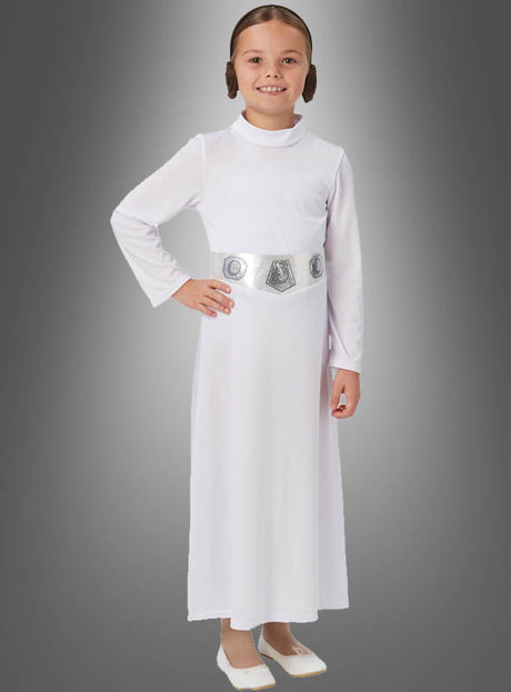 Vor einem grauen Hintergrund mit Farbverlauf steht ein lächelndes Kind, gekleidet im STAR WARS Prinzessin-Leia-Kinderkostüm mit einem langen weißen Kleid, einem silbernen Gürtel und weißen Schuhen – perfekt für den Kinderfasching oder jede andere Star-Wars-Kostümparty.