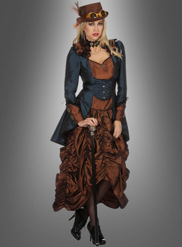 Eine Frau im Steampunk-Damenkleid „Lady Philippa Blue“: ein braun-marineblaues Kleid mit einer Korsettjacke, einem Zylinder, der mit einer Schutzbrille und Federverzierungen geschmückt ist, dazu schwarze Stiefel und ein Spazierstock in der Hand vor grauem Hintergrund – ein Outfit, das an Lady Philippa Blue selbst erinnert.