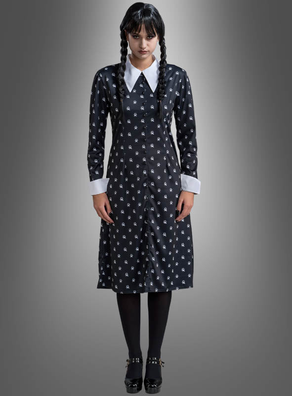 Eine Frau mit geflochtenen Zöpfen präsentiert das „Wednesday Damen Kleid schwarz-weiß“ – ein schwarzes Kleid mit weißem Kragen und weißen Manschetten, kombiniert mit schwarzen Strumpfhosen und Schuhen –, vor einem grauen Hintergrund mit Farbverlauf – ideal für alle, die ein Wednesday-Kostüm oder ein Addams-Family-Kostüm im klassischen Stil suchen.