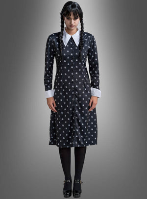 Eine Frau mit geflochtenen Zöpfen präsentiert das „Wednesday Damen Kleid schwarz-weiß“ – ein schwarzes Kleid mit weißem Kragen und weißen Manschetten, kombiniert mit schwarzen Strumpfhosen und Schuhen –, vor einem grauen Hintergrund mit Farbverlauf – ideal für alle, die ein Wednesday-Kostüm oder ein Addams-Family-Kostüm im klassischen Stil suchen.