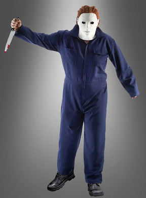 Eine Person, gekleidet in einem „Michael M. Overall Herren“-Halloween-Kostüm, einer weißen Maske und schwarzen Stiefeln, hält ein großes Messer mit roten Flecken auf der Klinge in der Hand und steht vor einem schlichten, grau verlaufenden Hintergrund.