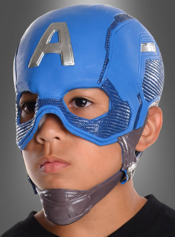 Ein Kind, das eine blaue „Deluxe Captain America“-Kindermaske mit einem „A“ auf der Stirn trägt, blickt mit ausdruckslosem Gesicht vor sich hin, vor einem grauen Hintergrund.