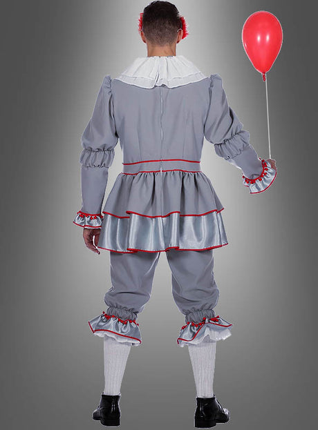 Eine Person, die das Halloween-Clown-Kostüm trägt – aus grauem Stoff mit Rüschen und roten Borten –, hält einen roten Luftballon in der Hand und steht mit dem Rücken zur Kamera.