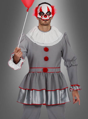 Eine Person im Halloween-Clown-Kostüm – aus grauem Stoff mit roten Verzierungen und Knöpfen – hält einen roten Luftballon in der Hand und trägt eine furchteinflößende weiß-rote Clownmaske mit leuchtend roten Haarbüscheln, während sie vor einem grauen Hintergrund steht. Dieses auffällige Outfit eignet sich perfekt für Halloween oder als unvergessliches Clown-Kostüm für Herren für jede gruselige Veranstaltung.