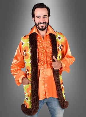 Ein Mann, der ein orangefarbenes Rüschenhemd und die „70er Retroweste Herren grün-braun“ trägt – eine im Vintage-Stil gehaltene, grün-braune Retro-Weste mit braunem Kunstfellbesatz –, steht vor einem grauen Hintergrund mit Farbverlauf.