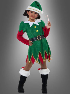 Ein Kind, das das „Süße Weihnachtselfe“-Kinderkostüm trägt – komplett mit Mütze, schwarzen Stiefeln und einem Gürtel –, steht vor einem grauen Hintergrund und hält eine Zuckerstange in der Hand.