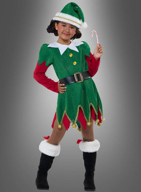 Ein Kind, das das „Süße Weihnachtselfe“-Kinderkostüm trägt – komplett mit Mütze, schwarzen Stiefeln und einem Gürtel –, steht vor einem grauen Hintergrund und hält eine Zuckerstange in der Hand.