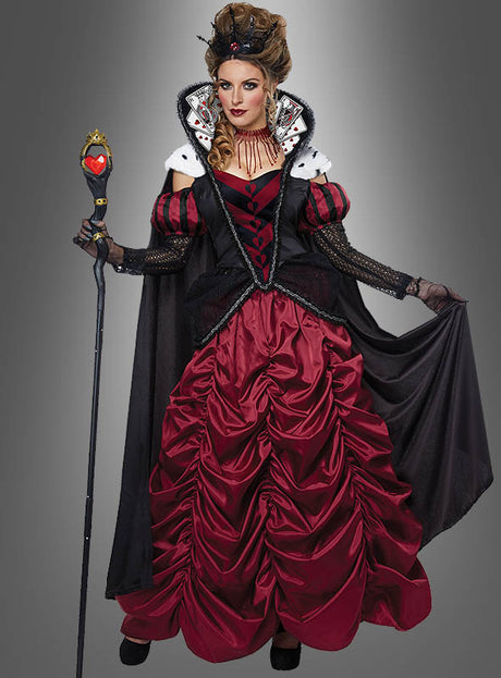Eine Frau im „Herzkönigin“-Kostüm-Ballkleid Deluxe – einem auffälligen rot-schwarzen Abendkleid – trägt eine Krone, hält ein Zepter in der Hand und präsentiert sich mit dramatischem Make-up vor einem grauen Hintergrund.