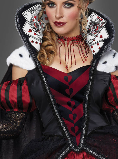 Eine Frau in einem „Herzkönigin“-Kostüm, einem Ballkleid der Deluxe-Ausführung, mit Spielkarten am Kragen, einem auffälligen rot-schwarzen Kleid und einer markanten roten Perlenkette.