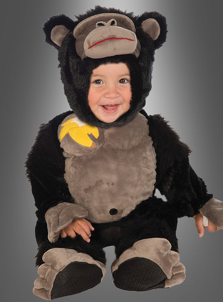Ein lächelndes Kind trägt den „Gorilla Affenkostüm“-Strampler für Babys, der ein schwarz-graues Design mit einem Bananen-Aufnäher auf der Schulter aufweist, und sitzt vor einem grauen Hintergrund mit Farbverlauf.