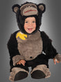 Ein lächelndes Kind trägt den „Gorilla Affenkostüm“-Strampler für Babys, der ein schwarz-graues Design mit einem Bananen-Aufnäher auf der Schulter aufweist, und sitzt vor einem grauen Hintergrund mit Farbverlauf.