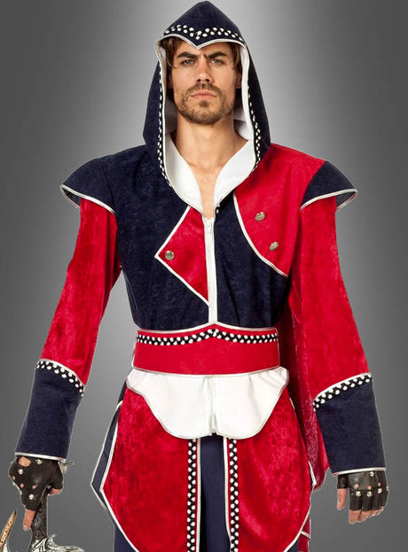 Ein Mann, der das „Fantasy Krieger Ezio“-Herrenkostüm trägt – ein mittelalterliches Design mit Kapuze, aus rotem und marineblauem Samt mit weißen Akzenten und silbernen Nietenbesätzen –, steht vor einem schlichten grauen Hintergrund.