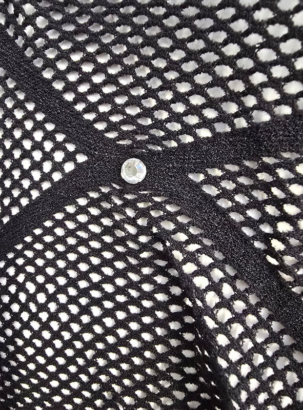 Nahaufnahme des schwarzen Stoffes „Stylische Strumpfhose mit Glitzersteinchen“, der von schwarzen Bändern durchzogen ist, die ein X bilden, in dessen Mitte sich ein kleiner runder Nietenstift befindet.