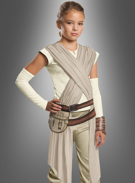 Ein junges Mädchen trägt das „Rey Star Wars Deluxe“-Kinderkostüm in Beige und Braun, das von der legendären Science-Fiction-Figur inspiriert ist, und steht selbstbewusst vor einem schlichten grauen Hintergrund.