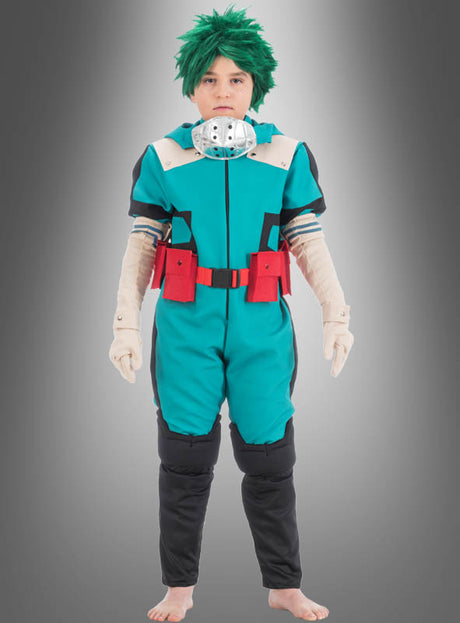 Eine Person mit einer grünen Perücke und einem blaugrünen Overall mit roten Akzenten sowie Handschuhen steht barfuß vor einem grauen Hintergrund mit Farbverlauf und ist als Anime-Figur in einem Izuku-Midoriya-Kostüm aus „My Hero Academia“ verkleidet.