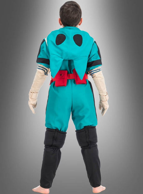 Ein Kind trägt das Izuku-Midoriya-Kostüm für Kinder aus „My Hero Academia“ in den Farben Blaugrün und Schwarz mit einem roten Gürtel. Es steht barfuß vor einem grauen Hintergrund und ist mit dem Rücken zur Kamera gewandt.