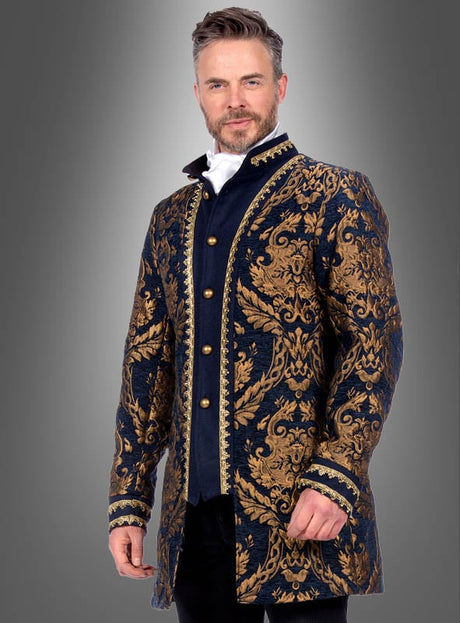 Ein Mann, der eine „Deluxe Barock Brokatjacke Herren“ in Marineblau und Gold mit kunstvollen Mustern und goldenen Knöpfen über einem weißen Hemd trägt, steht vor einem grauen Hintergrund mit Farbverlauf.