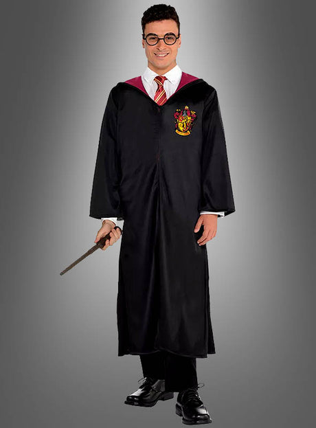Eine Person, die ein Harry-Potter-Kostüm für Erwachsene mit Zauberstab trägt – bestehend aus einer schwarzen Gryffindor-Robe mit rot-goldenem Wappen, einem weißen Hemd, einer rot gestreiften Krawatte und einer Brille – und einen Zauberstab in der Hand hält, steht vor einem schlichten grauen Hintergrund.