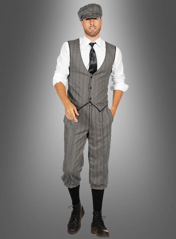 Ein Mann im „20er-Kostüm Finn mit Knickerbocker“ – bestehend aus einer grauen Zeitungsjungenmütze, einer grauen Weste und einer Knickerbocker-Hose, dazu ein weißes Hemd, eine schwarze Krawatte, schwarze Socken und braune Stiefel – posiert vor einem schlichten grauen Hintergrund.