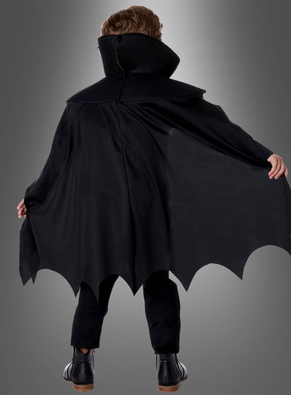 Ein Kind, das das Edler Dracula-Kostüm für Kinder trägt – mit schwarzem Umhang, hohem Kragen und gewellten Säumen –, steht mit dem Rücken zur Kamera und streckt die Arme aus wie ein klassischer Vampir.